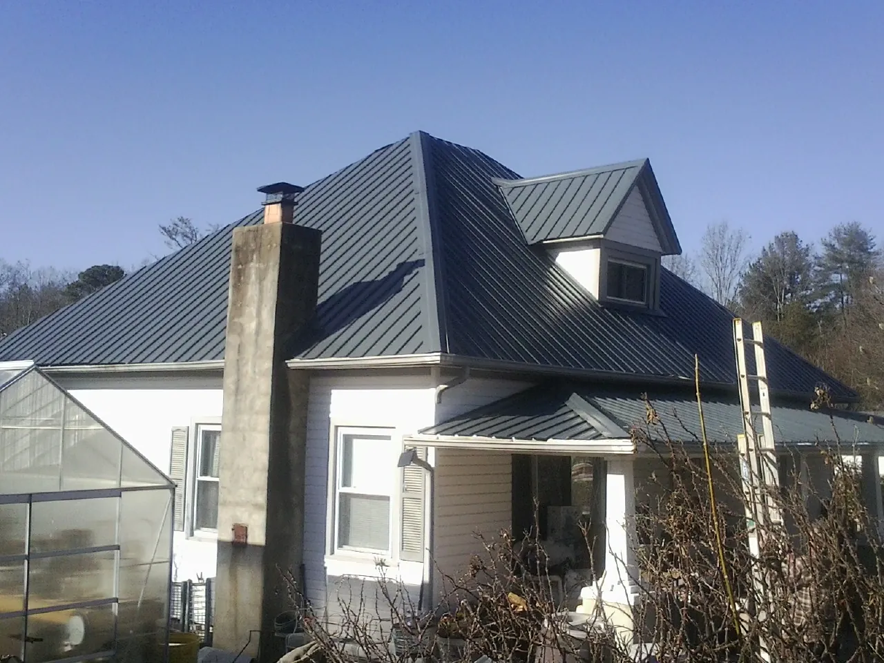 Dark blue standing seam metal roof on a white farmhouse with dormer — Slate & Tile Roof Repair by Roofing Brothers in North Salt Lake