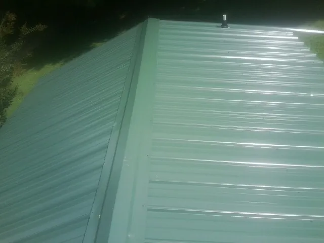 New green metal panels meeting at the ridge of a roof — Flat Roof Repair work by our crew in North Salt Lake