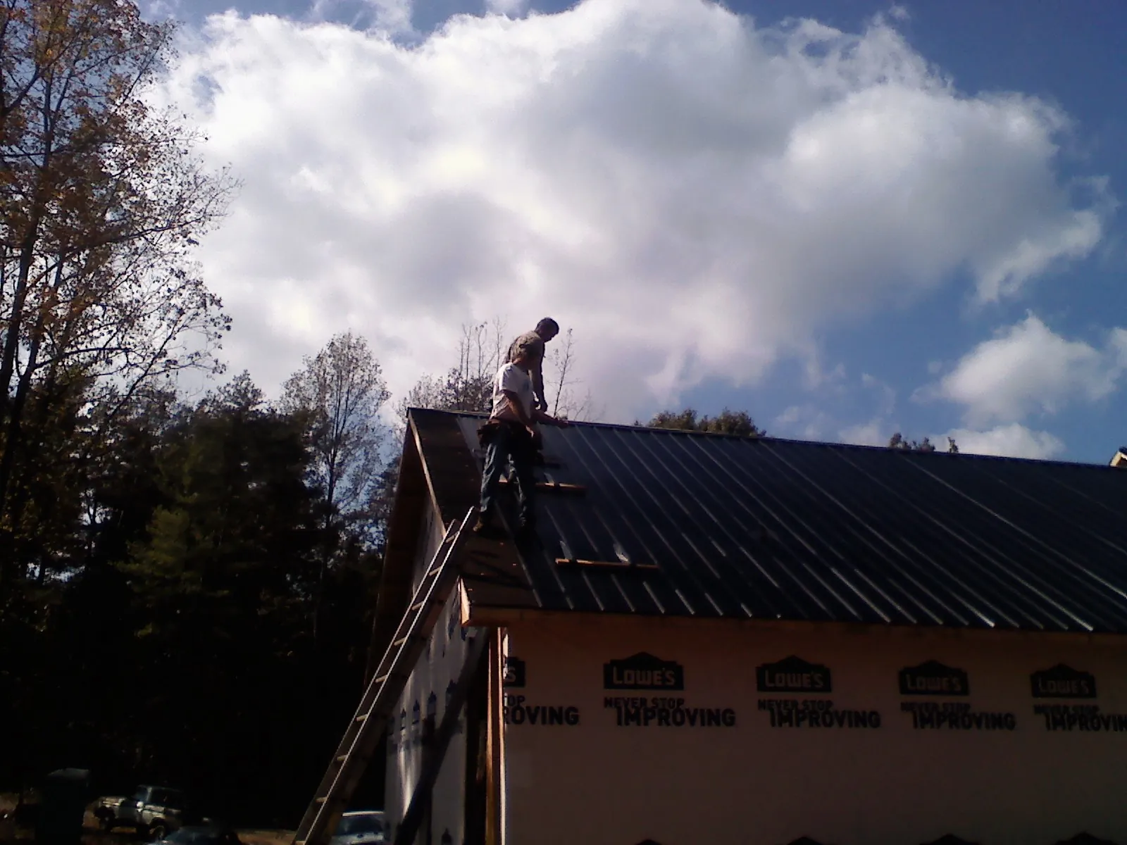 Roofer fastening dark metal panels high against a cloudy sky, from a Roof Inspection job in North Salt Lake