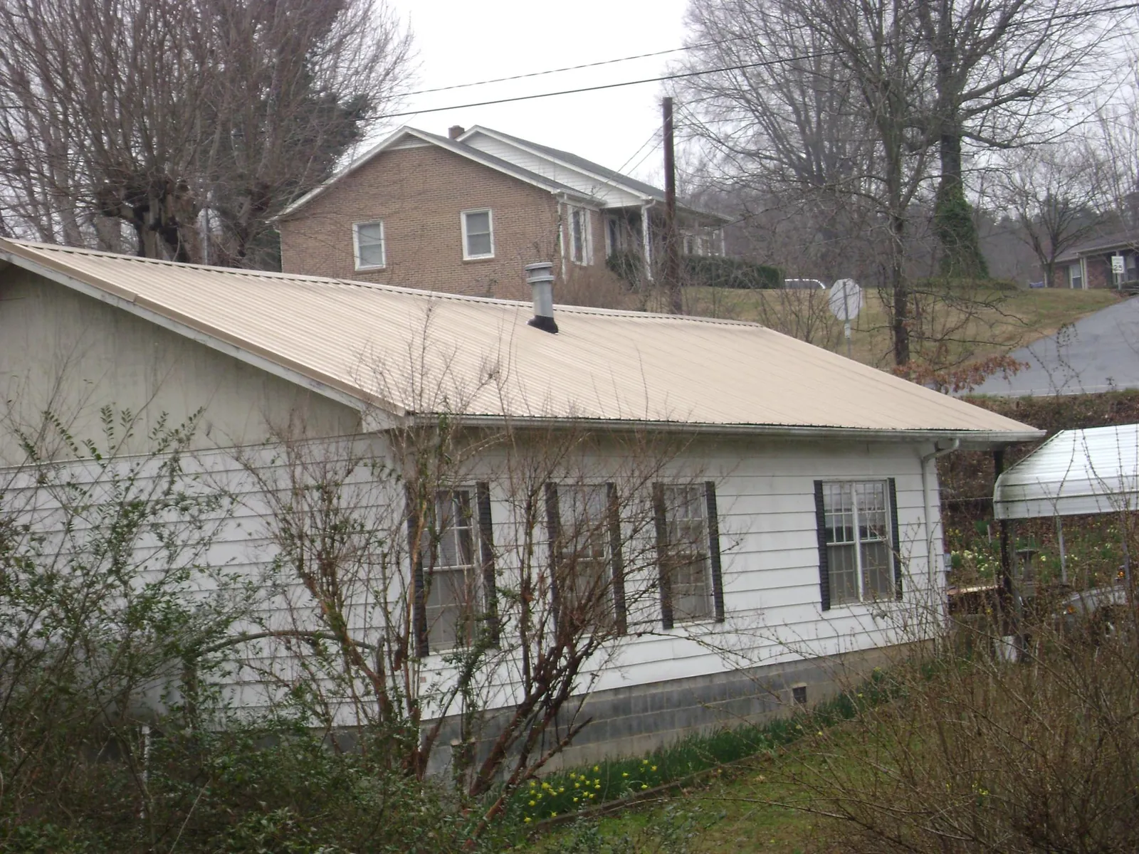 Tan metal roof on a white sided house set into a hillside — Commercial Roofing by Roofing Brothers in North Salt Lake
