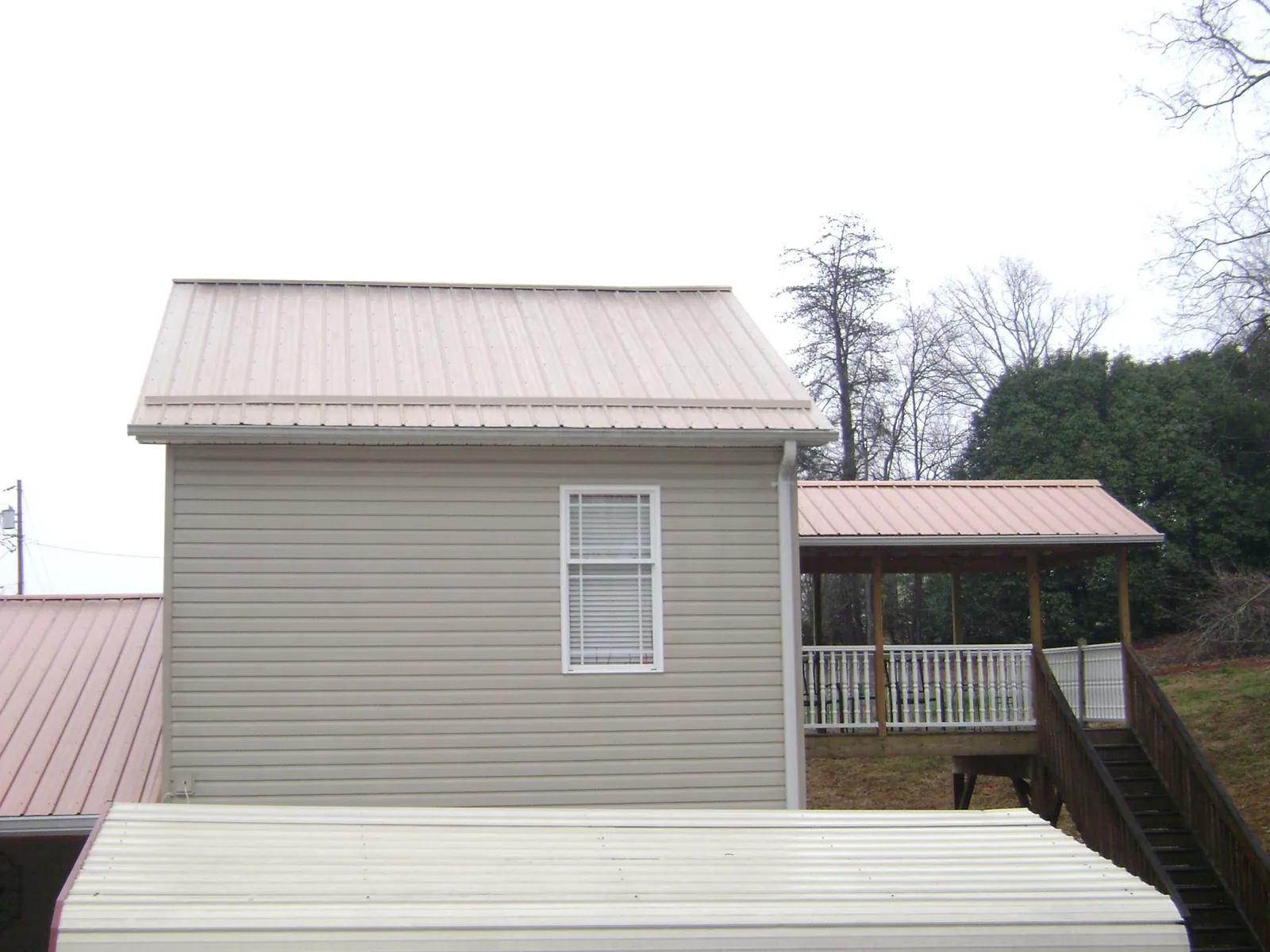 Tan metal roofs on a two story addition and attached porch, from a Roof Replacement job in North Salt Lake